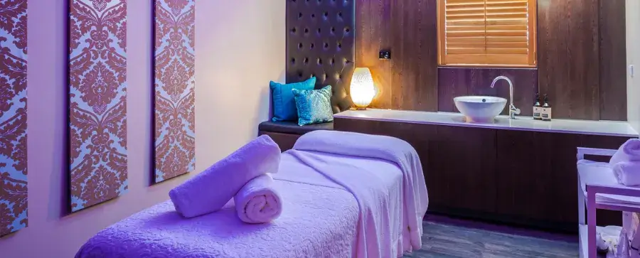 Spa treatment room with massage table, sink, and decorative wallpaper. 